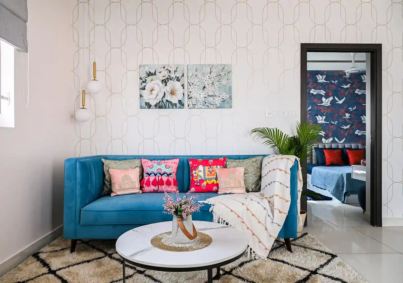 A modern living room with a blue-toned soft sofa with colorful and multi-patterned pillows. Also, a marbled coffee table