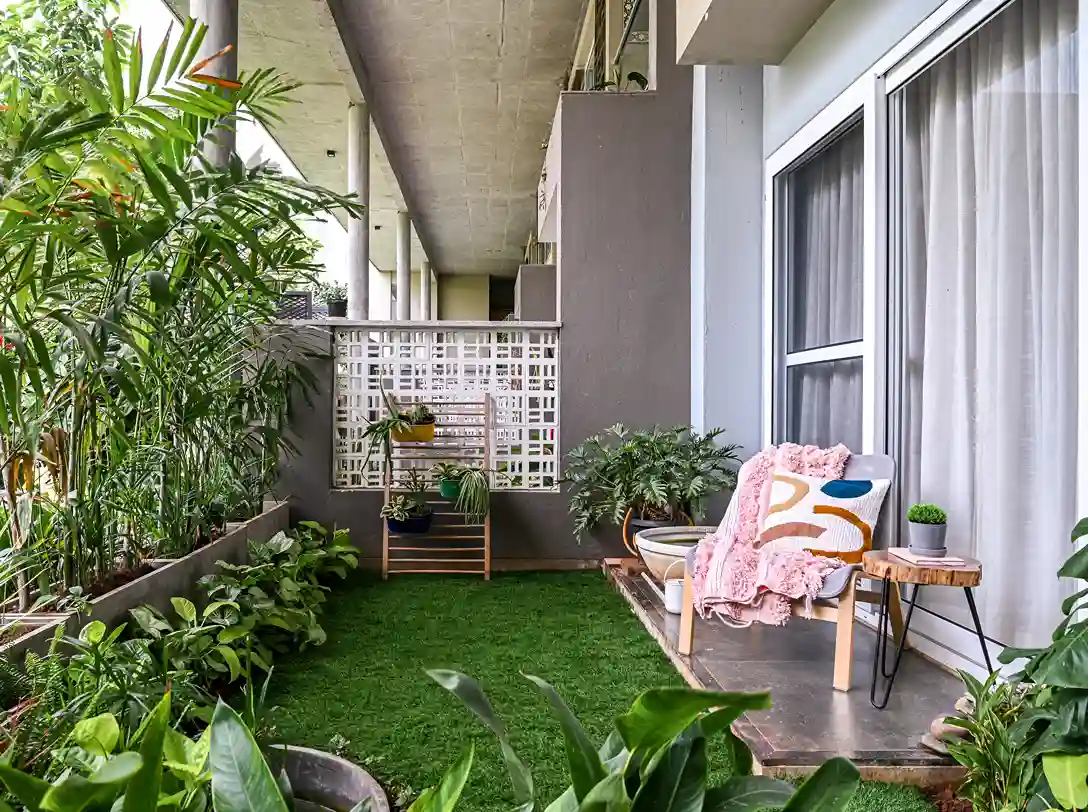 A cozy balcony garden featuring vibrant green plants, a comfortable chair with a blanket, and decorative elements against a modern backdrop.